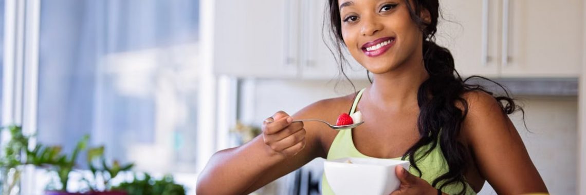 Smiling young woman in sportswear enjoying a healthy fruit snack indoors.